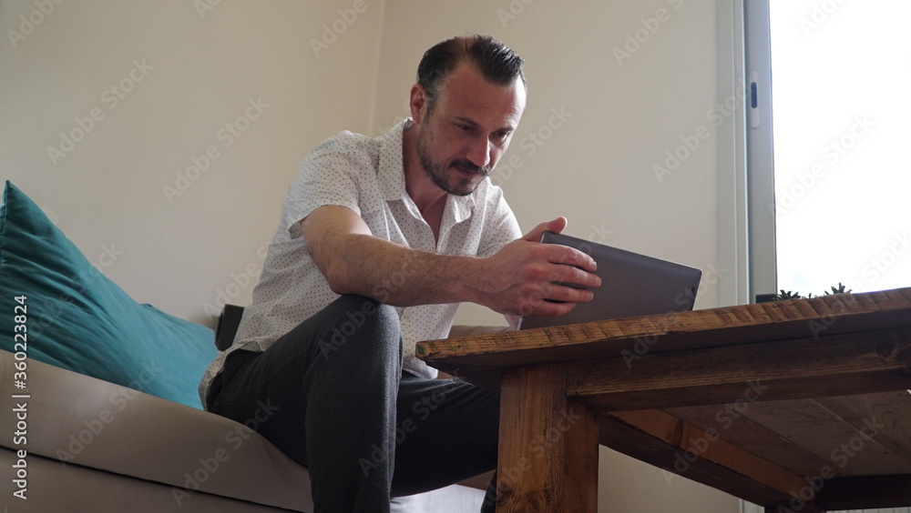 Happy man relaxing on couch while video calling using laptop at home. man sitting on sofa and making a video call. Smiling businessman doing online video.
