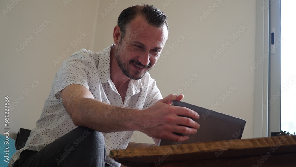 Happy man relaxing on couch while video calling using laptop at home. man sitting on sofa and making a video call. Smiling businessman doing online video. Happy man relaxing on couch while video calling using laptop at home. man sitting on sofa and making a video call. Smiling businessman doing online video.
