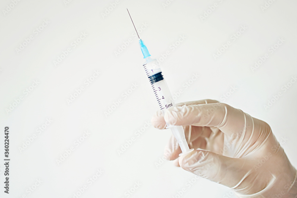 The doctor's hand in a medical glove holds a syringe. Vaccination. Prevention and treatment of diseases. Coronavirus. High quality photo. Epidemic. Space for text The doctor's hand in a medical glove holds a syringe. Vaccination. Prevention and treatment of diseases. Coronavirus. High quality photo. Epidemic. Space for text