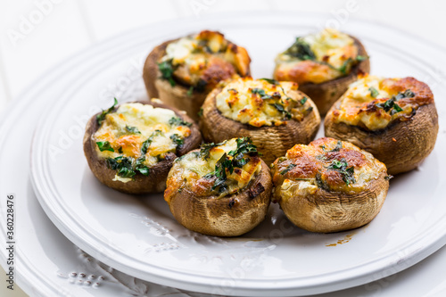 Baked champignons, filled with cheese, parsley and roasted garlic on white plate.