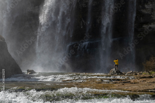 Adventure man looking at Tortum Waterfall in Turkey. Tourist in a yellow jacket relaxing at the Tortum waterfall in Turkey. Landscape view of Tortum Waterfall in Erzurum,Turkey