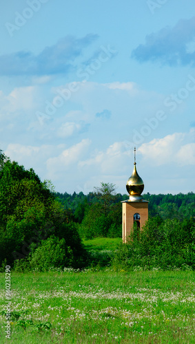Orthodox chapel among the green forest against a clear sky. Vertical format.