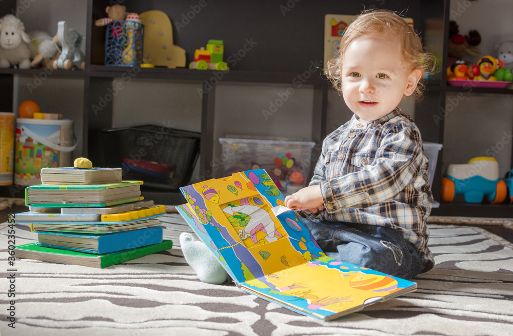 Fototapeta premium Happy sweet child reading books sitting on the floor, at home