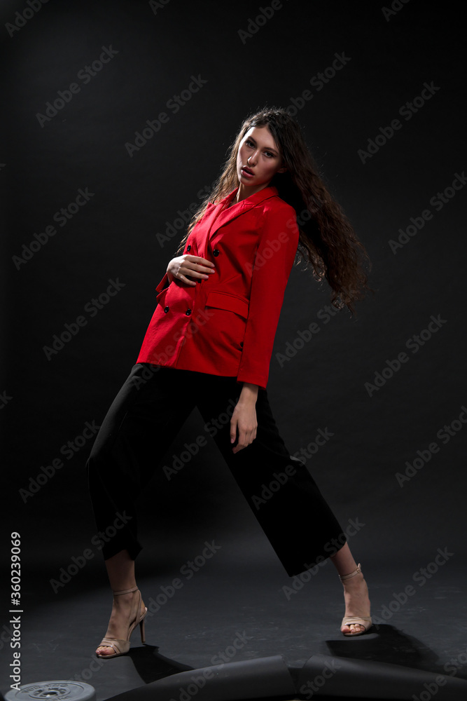 A young beautiful oriental woman with long black hair in a red jacket against a black background. The fashion model poses in the studio.