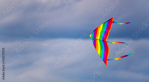 A bright multi-colored kite flies in the air against a cloudy evening summer sky