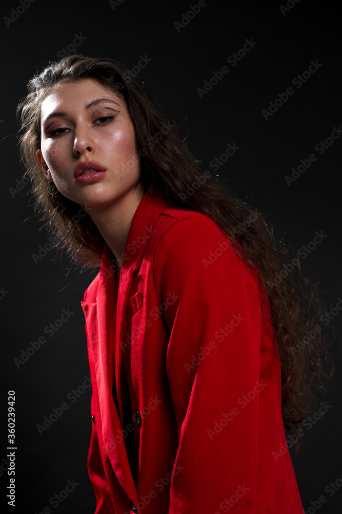A young beautiful oriental woman with long black hair in a red jacket against a black background. The fashion model poses in the studio. A young beautiful oriental woman with long black hair in a red jacket against a black background. The fashion model poses in the studio.