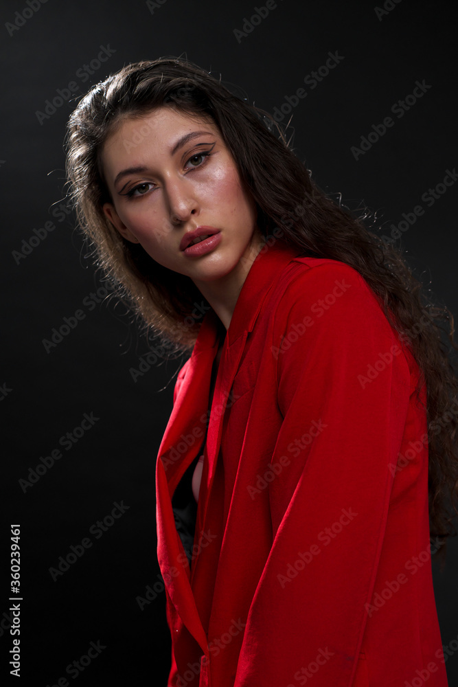 A young beautiful oriental woman with long black hair in a red jacket against a black background. The fashion model poses in the studio. A young beautiful oriental woman with long black hair in a red jacket against a black background. The fashion model poses in the studio.