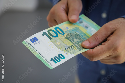 euro banknotes holding in both hands, young men pay with hundred euro bill, unemployed and poor in germany or europe, horizontal