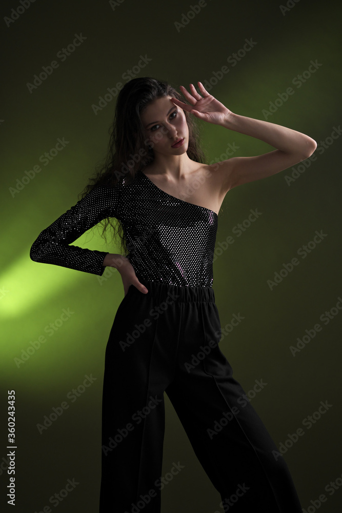 A beautiful young tall girl with long black hair poses in a shiny blouse and black culottes on a green background. Buty and fashion photo shoot. A beautiful young tall girl with long black hair poses in a shiny blouse and black culottes on a green background. Buty and fashion photo shoot.