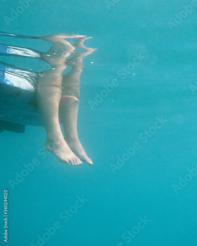 Underwater photo of two feet hanging down from a kayak. Stock photo of a person sitting in a kayak with her feet in the water shoot from below.