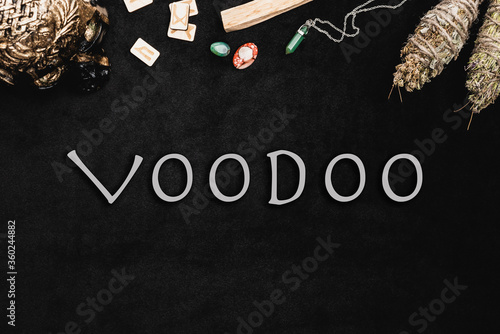 Top view of voodoo lettering near runes, amulets and crystals on black
