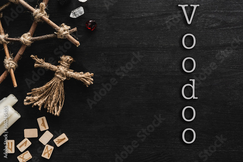 top view of voodoo dolls, ancient runes, pentagram, candles and crystals near voodoo lettering on black