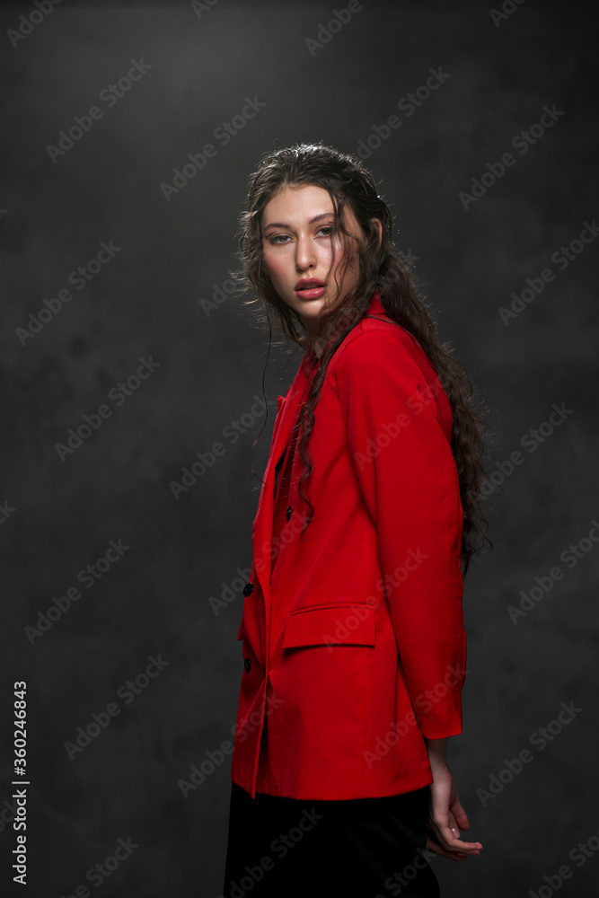 A young beautiful oriental woman with long black hair in a red jacket against a black background. The fashion model poses in the studio. A young beautiful oriental woman with long black hair in a red jacket against a black background. The fashion model poses in the studio.