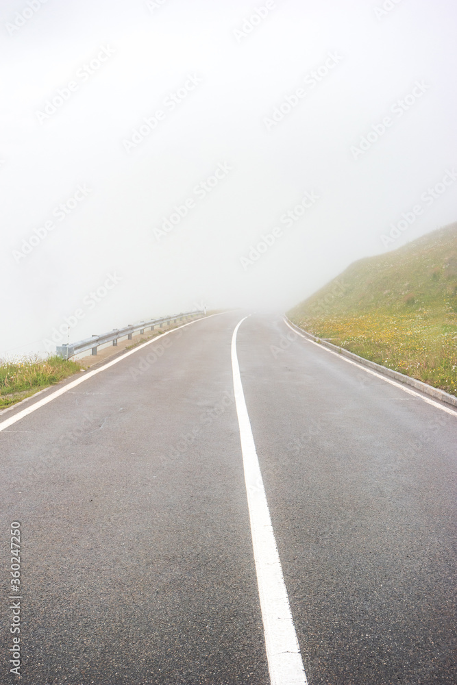 Asphalt paved mountain road covered in fog no cars or people