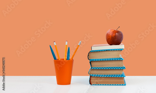 Back to school, pile of books and red apple on the white table with pink orange background. Distance home education. Quarantine concept of stay home. © Inna