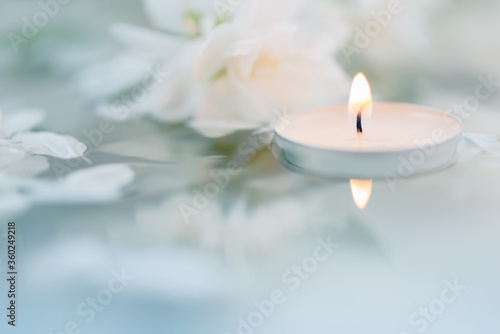 White candle with flowers float on the surface of the water. Focused on the flame of the candle. SPA. CloseUp. Macro, Defocused. ReflectiCloseUp. Macro, Defocused. Focused on the flame of the candle.