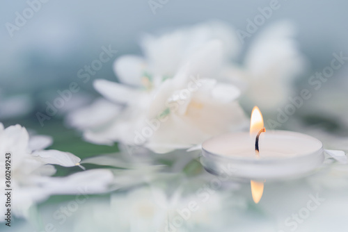 White candle with flowers float on the surface of the water.  Focused on the flame of the candle. SPA. CloseUp. Macro  Defocused. ReflectiCloseUp. Macro  Defocused. Focused on the flame of the candle.