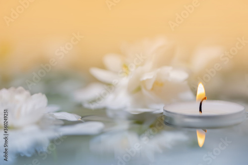 White candle with flowers float on the surface of the water. Focused on the flame of the candle. SPA. CloseUp. Macro, Defocused. Reflections.