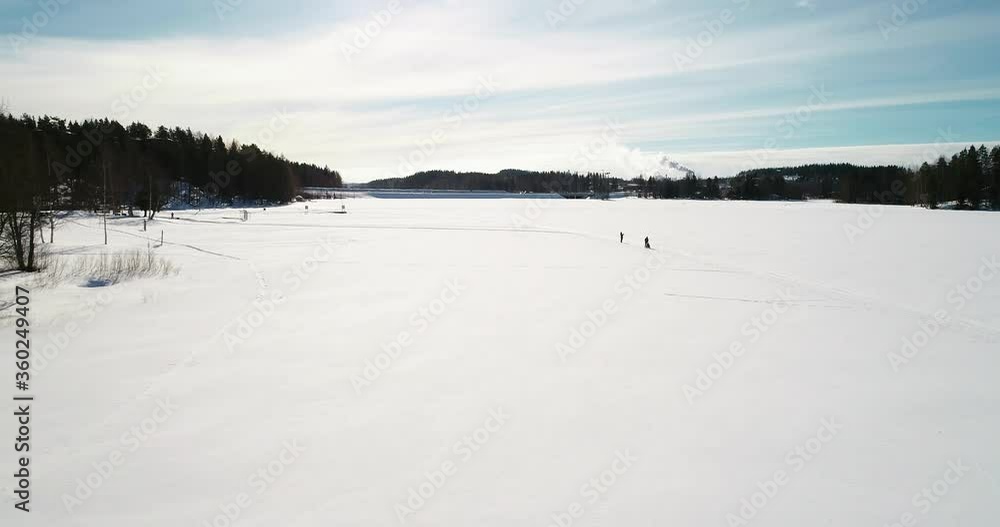 Aerial , drone shot passing people hiking on snow covered ice path, at a polar lake, on a bright, sunny winter day, in Kemijarvi, Finland Aerial , drone shot passing people hiking on snow covered ice path, at a polar lake, on a bright, sunny winter day, in Kemijarvi, Finland