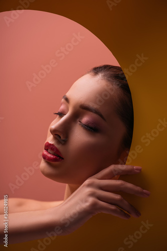 naked beautiful woman with crimson lips and closed eyes in paper circle hole in dark