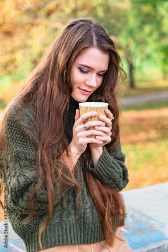 Girl enjoys smell of coffee sitting in autumn park