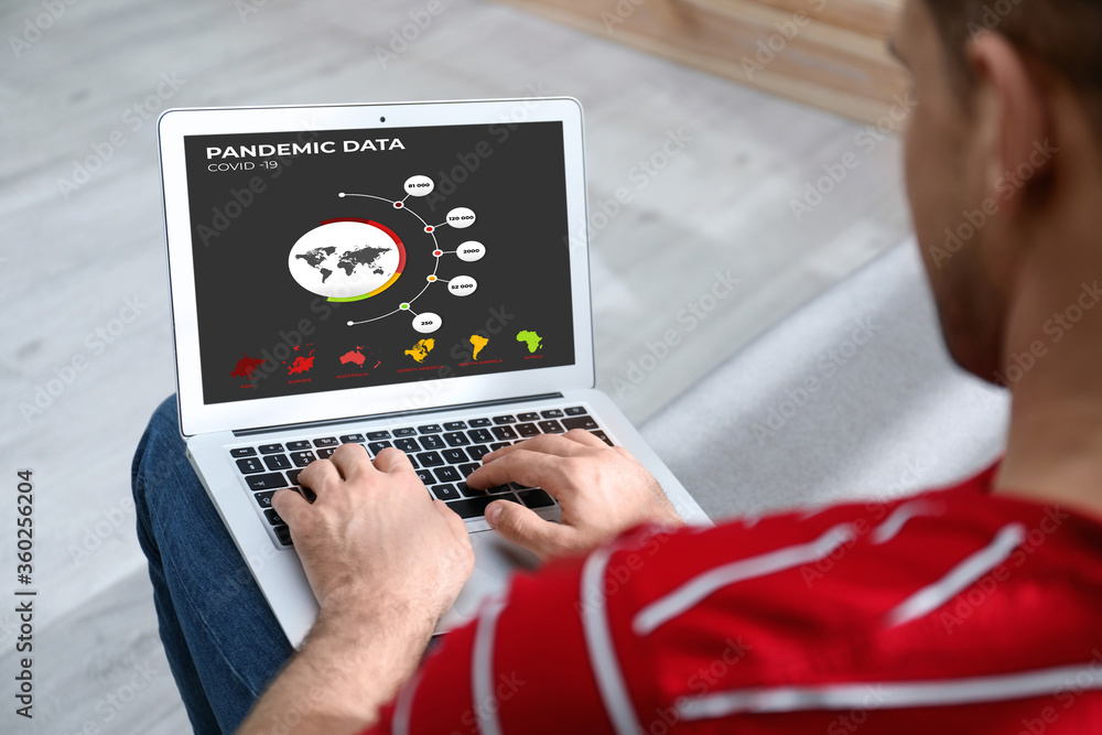 Man with laptop checking pandemic data indoors, closeup. Coronavirus outbreak