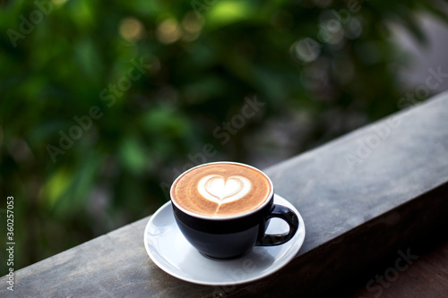 Black cup of tasty cappucino on white soucer with heart art latte. photo