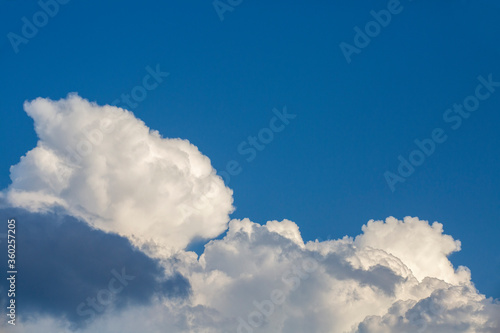 White contrasting clouds backlit by the sun on a blue summer sky. Background.