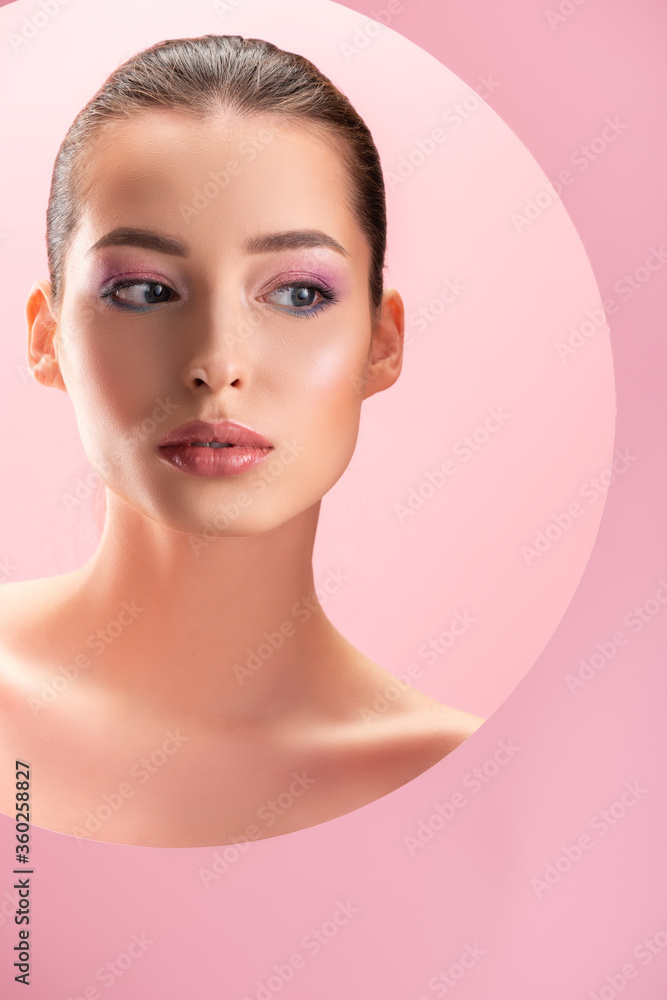 portrait of beautiful naked woman with shiny makeup looking through round paper hole isolated on pink portrait of beautiful naked woman with shiny makeup looking through round paper hole isolated on pink