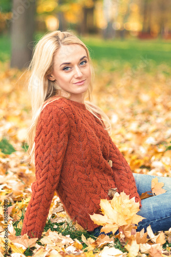 Beautiful young caucasian woman in red sweater sitting on the leaves in the autumn park