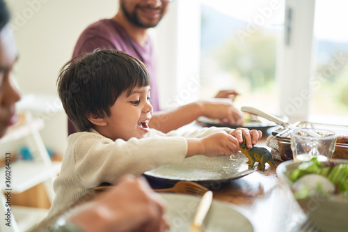 Happy boy playing with toy dinosaur at dinner table