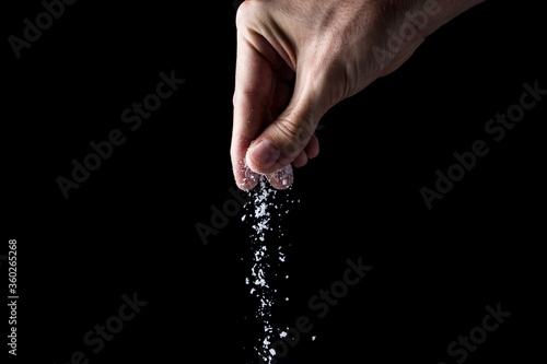 Male hand sprinkles salt on a black background. Cooking concept.