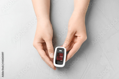 Woman holding fingertip pulse oximeter on light grey stone background, top view