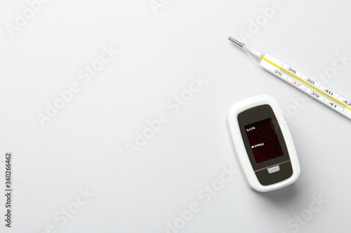 Modern fingertip pulse oximeter and mercury thermometer on white background, flat lay. Space for text