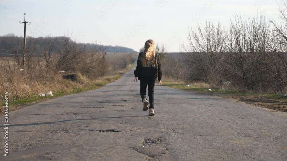 Rear view of little girl in jacket walks along empty road and dancing funny at sunny day. Small female child with long blonde hair haves fun on empty driveway at countryside. Slow motion Rear view of little girl in jacket walks along empty road and dancing funny at sunny day. Small female child with long blonde hair haves fun on empty driveway at countryside. Slow motion