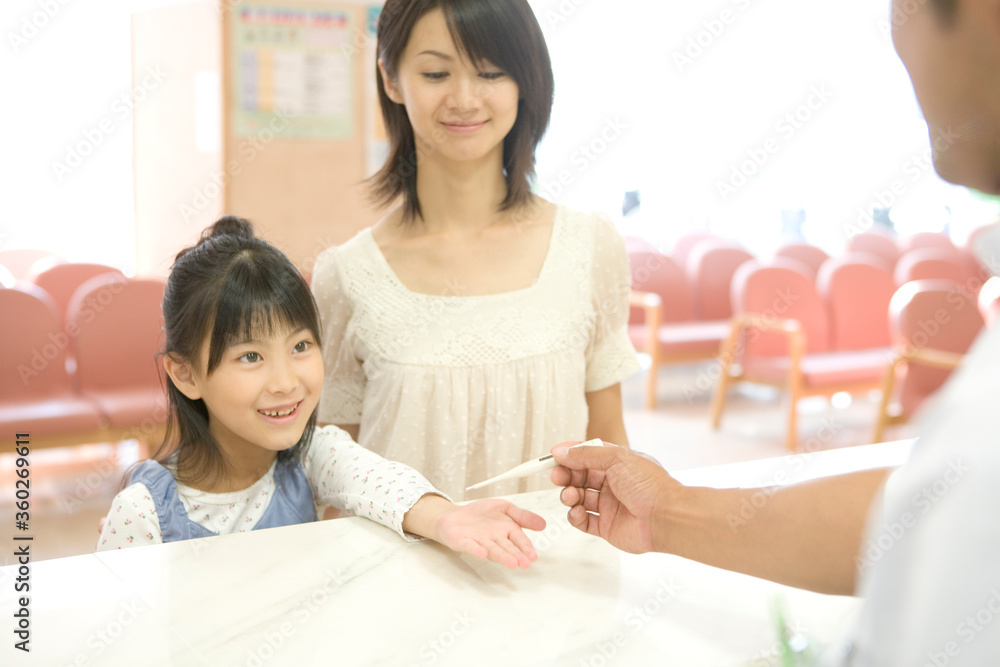 病院の受付で体温計を受け取る少女