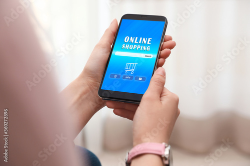 Woman holding smartphone with online shopping website on screen indoors, closeup