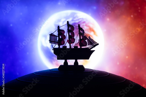 Beautiful boat toy over a blue balll with blurred blue and red planet and cosmos scene at background. Travel, universe and space concept photo