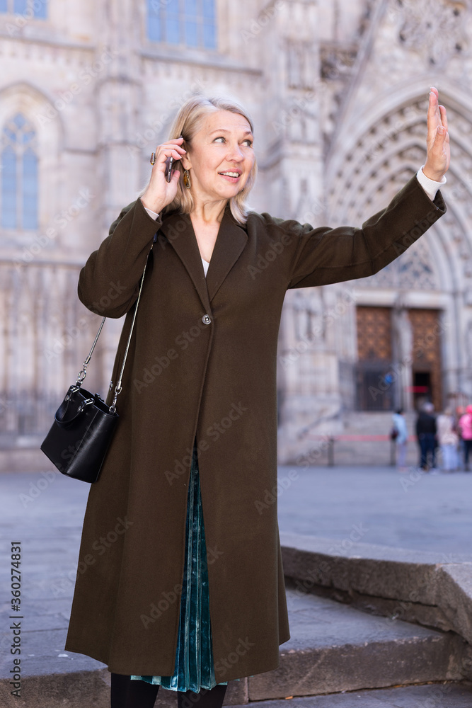 Adult woman talking on the phone and waving to someone on the street