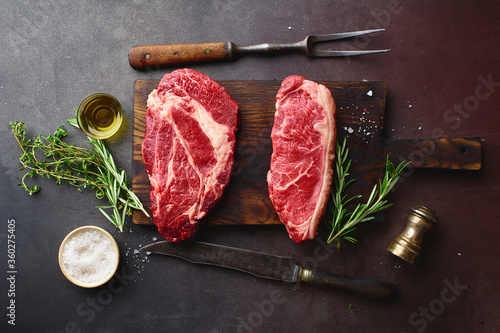 Top view of raw black angus prime beef steaks on wooden cutting board: chuck roll and striploin.
