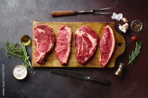 Top view of raw black angus prime beef steaks on wooden cutting board: rib eye, chuck roll, striploin and picanha. photo