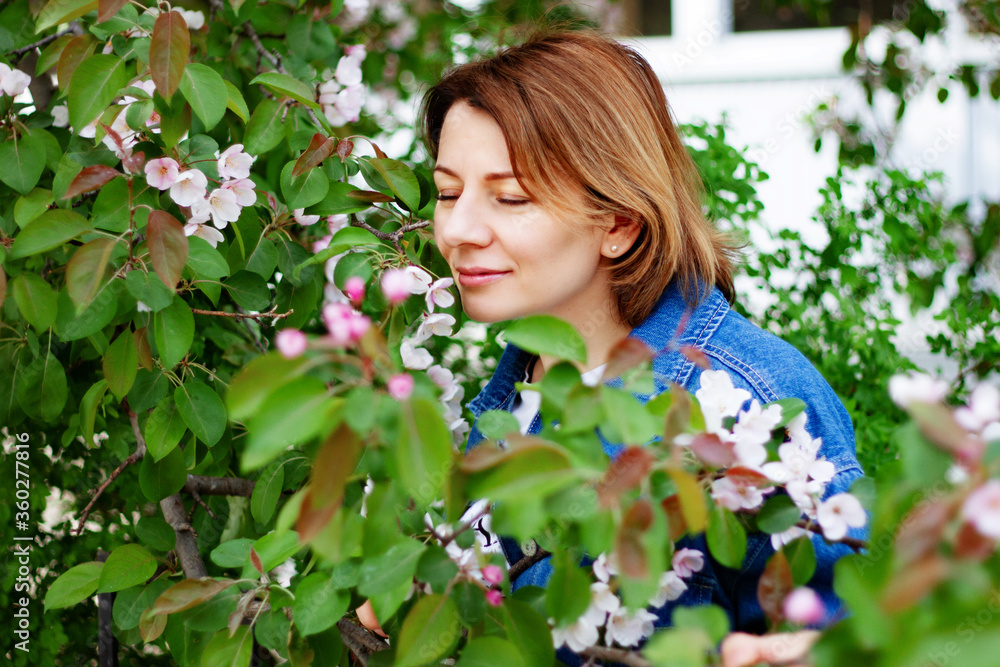 Beautiful brown haired woman with blue eyes in an Apple orchard sniffing blooming flowers on a spring day Beautiful brown haired woman with blue eyes in an Apple orchard sniffing blooming flowers on a spring day