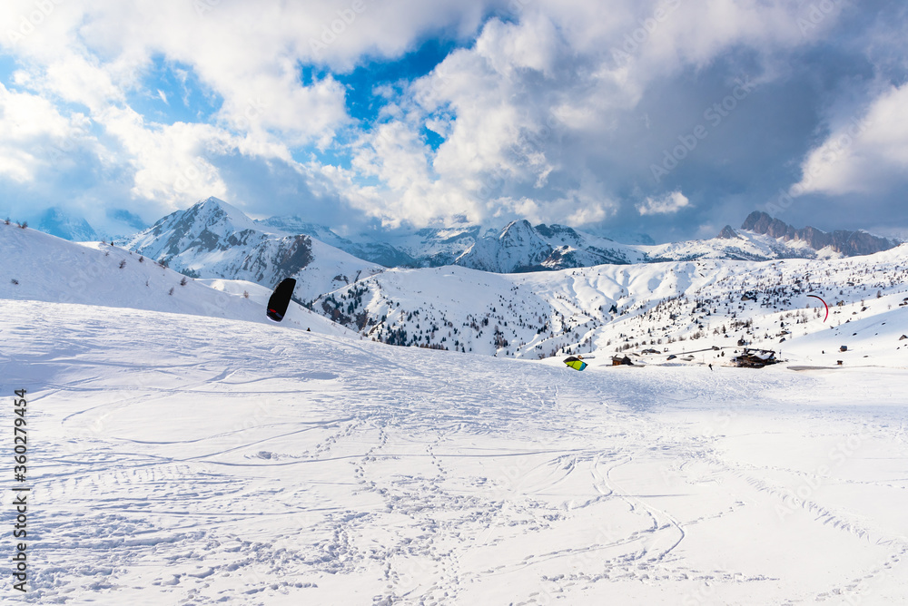 People kite skiing in a magnificent snowy mountain scenery in the European Alps on a sunny winter day