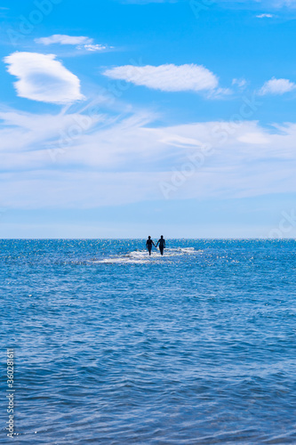 Couple holding hands walking alone towards the horizon in the middle of the sea on a sunny summer day. © Pol Solé