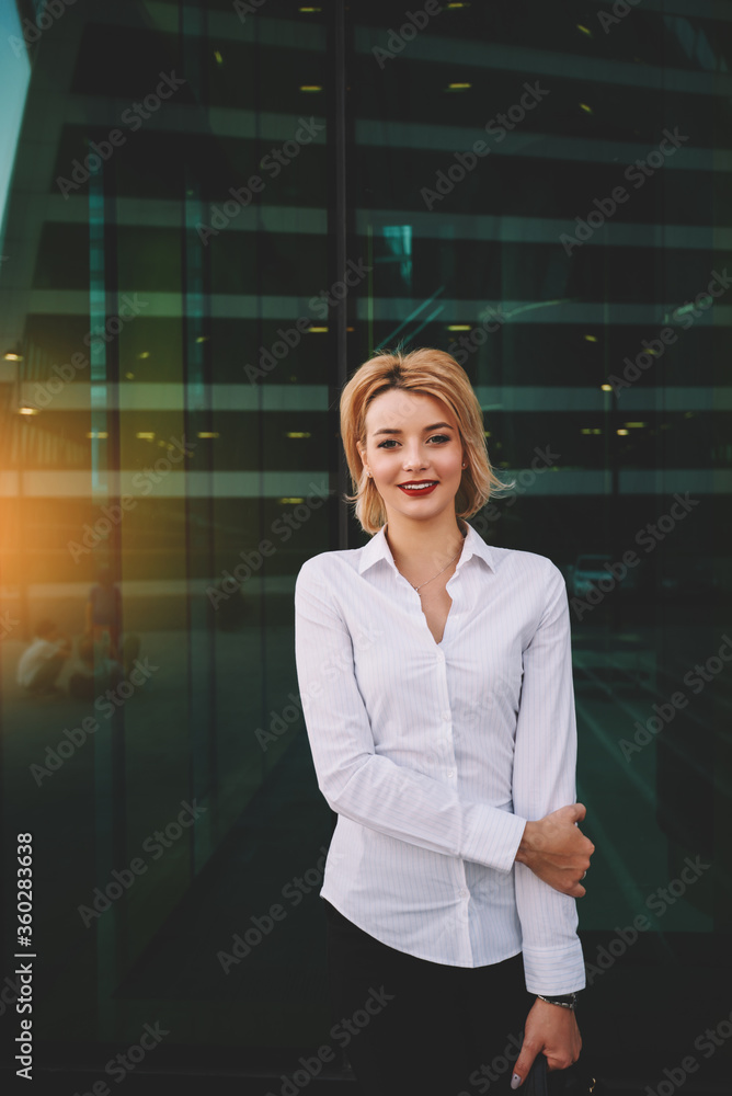 Young smiling woman secretary in real estate company is posing, while is waiting customers outside. Beautiful successful businesswoman is looking at camera, while is standing near office building Young smiling woman secretary in real estate company is posing, while is waiting customers outside. Beautiful successful businesswoman is looking at camera, while is standing near office building