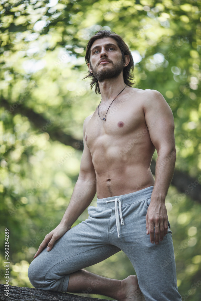 Shirtless man kneeling on branch at forest Shirtless man kneeling on branch at forest