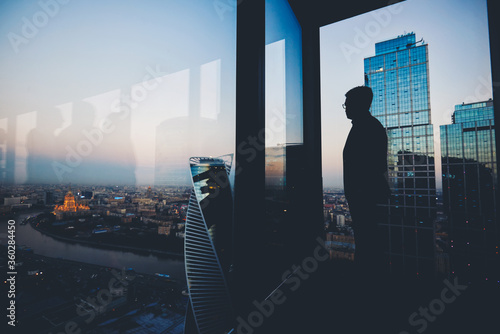 Silhouette of a man financier think about something while standing near office window background with copy space for your text message or advertising content, young male thoughtful rest after briefing