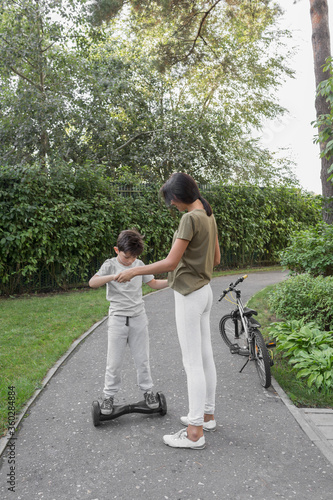 Mother assisting son in using self-balancing board on road against plants photo