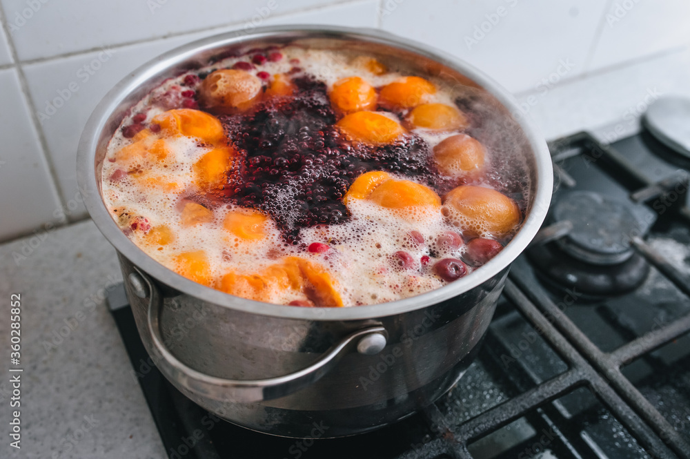 Cooking a delicious compote of apricot, apples, cherries, raspberries. Fresh fruits are boiled in boiling water in a metal pan on the stove. Photography, concept. Cooking a delicious compote of apricot, apples, cherries, raspberries. Fresh fruits are boiled in boiling water in a metal pan on the stove. Photography, concept.
