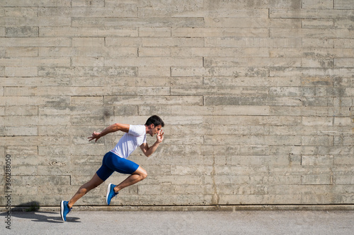 Billede på lærred Caucasian athlete making a start in front of an irregular grey wall background